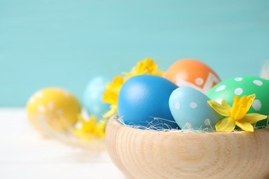 Photo of Colorful Easter eggs and flowers in wooden bowl on white table, closeup