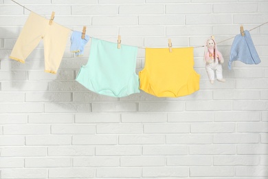 Baby clothes hanging on washing line near white brick wall