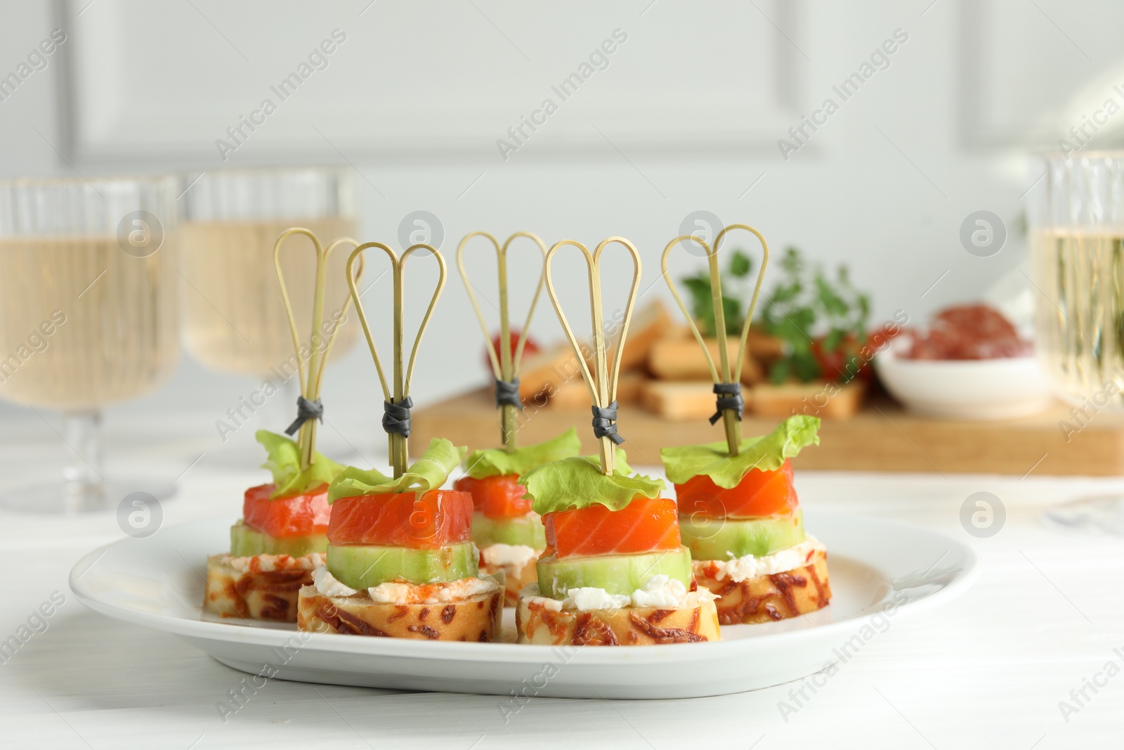 Photo of Tasty canapes with salmon, cucumber, bread and cream cheese on white wooden table