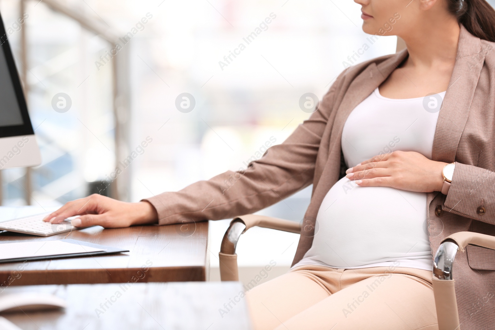 Photo of Young pregnant woman working with computer at table in office, closeup