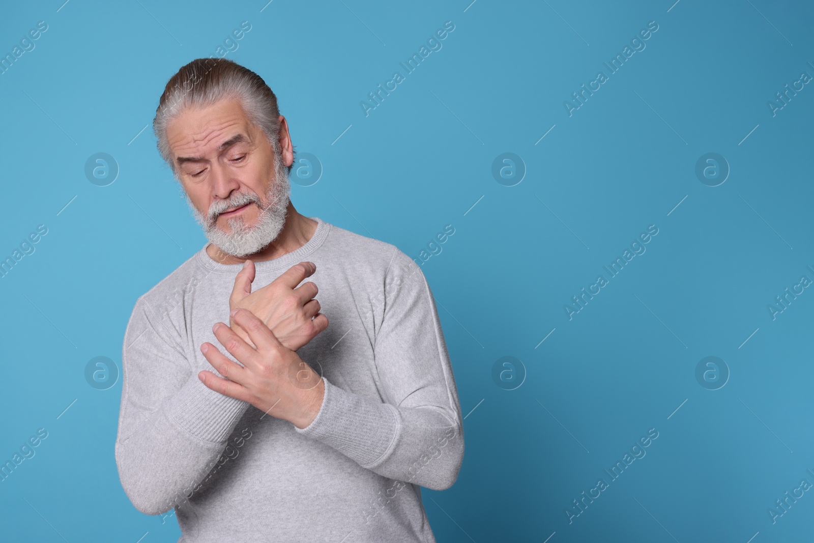 Photo of Senior man suffering from pain in hands on light blue background, space for text. Arthritis symptoms