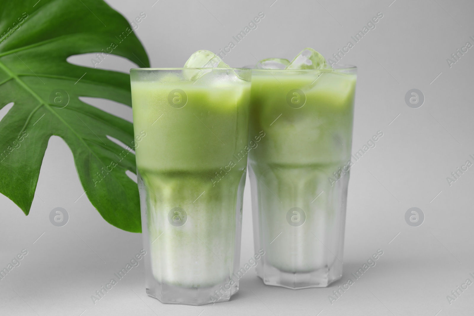 Photo of Glasses of tasty iced matcha latte and leaf on light grey background