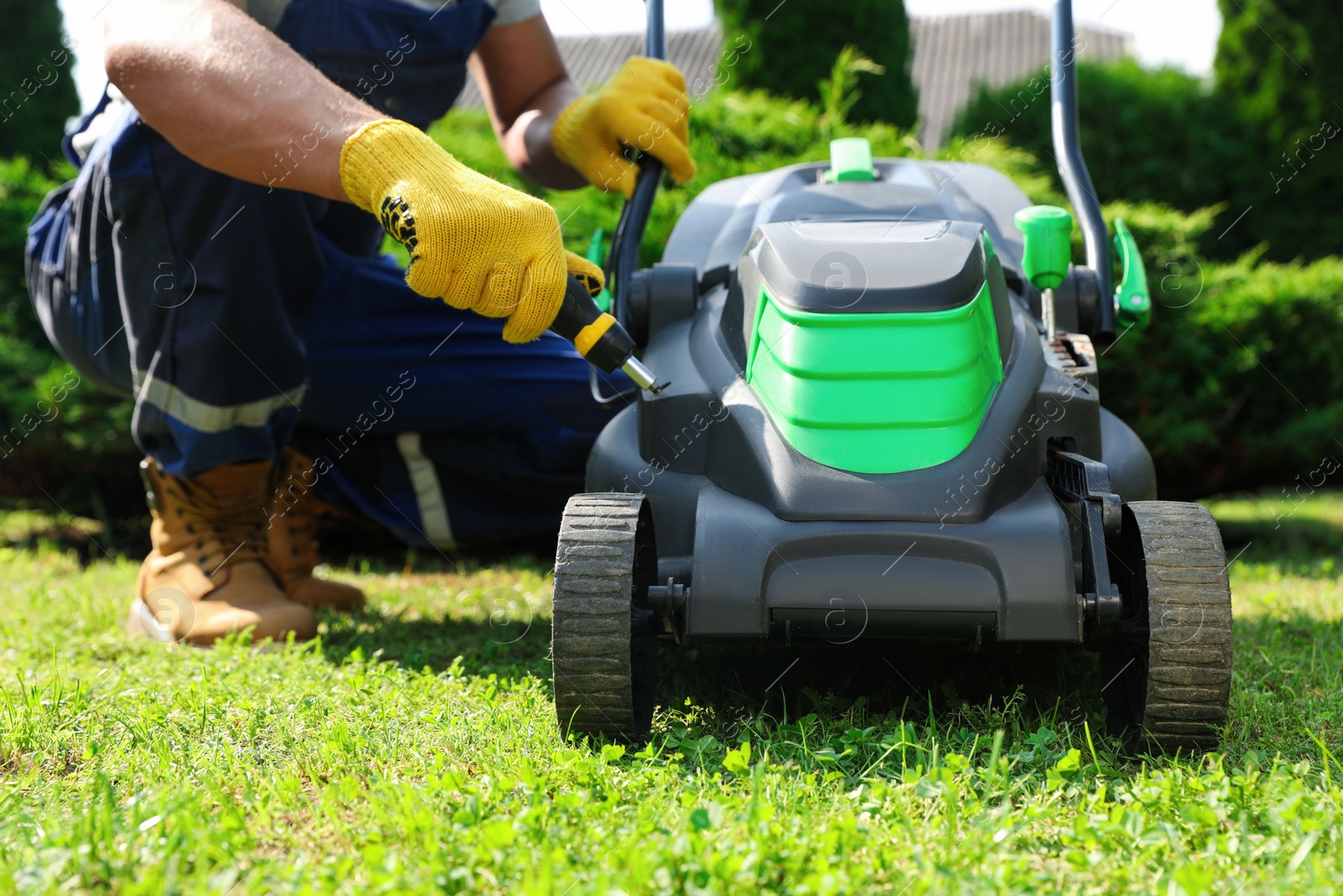 Photo of Young man with screwdriver fixing lawn mower in garden, closeup