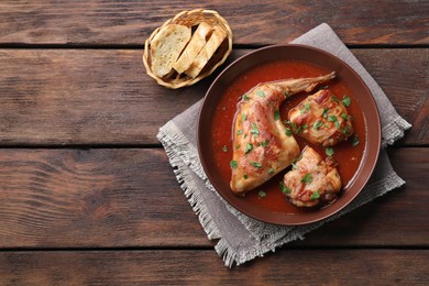Tasty cooked rabbit meat with sauce and bread on wooden table, top view. Space for text