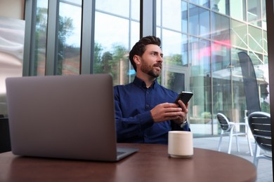 Photo of Man with smartphone and laptop at table in cafe