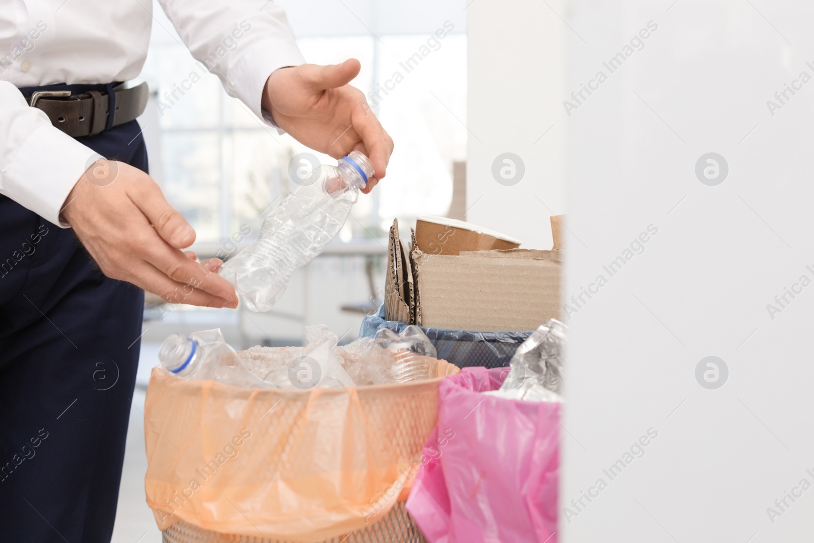 Photo of Man putting used plastic bottle into trash bin in office, closeup. Waste recycling