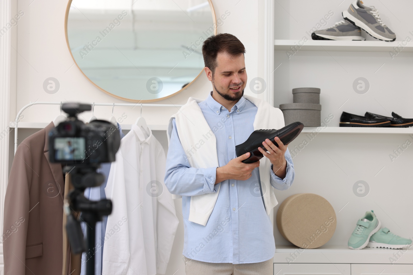 Photo of Smiling fashion blogger showing shoe while recording video at home