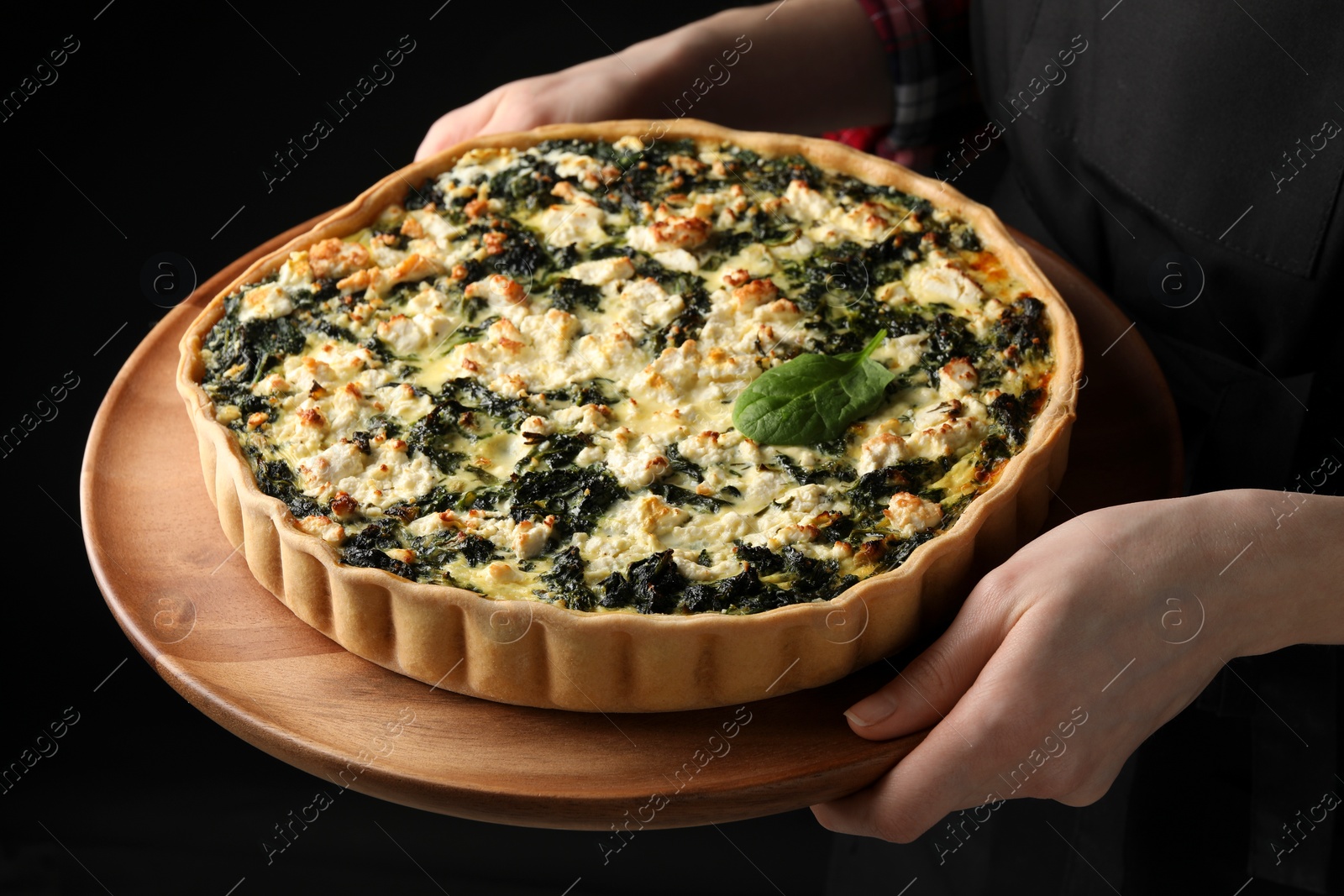 Photo of Woman holding delicious homemade spinach quiche on dark background, closeup