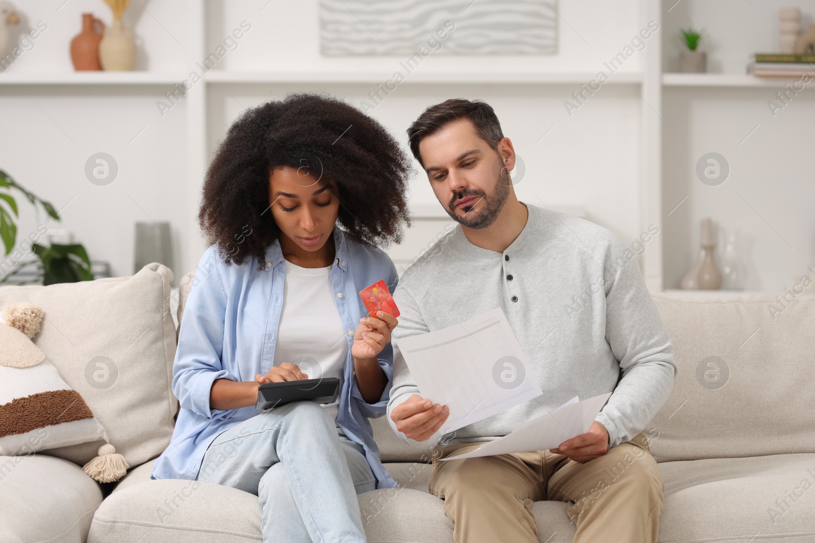 Photo of Confused couple with debt notifications, calculator and credit card planning budget at home. Financial problem