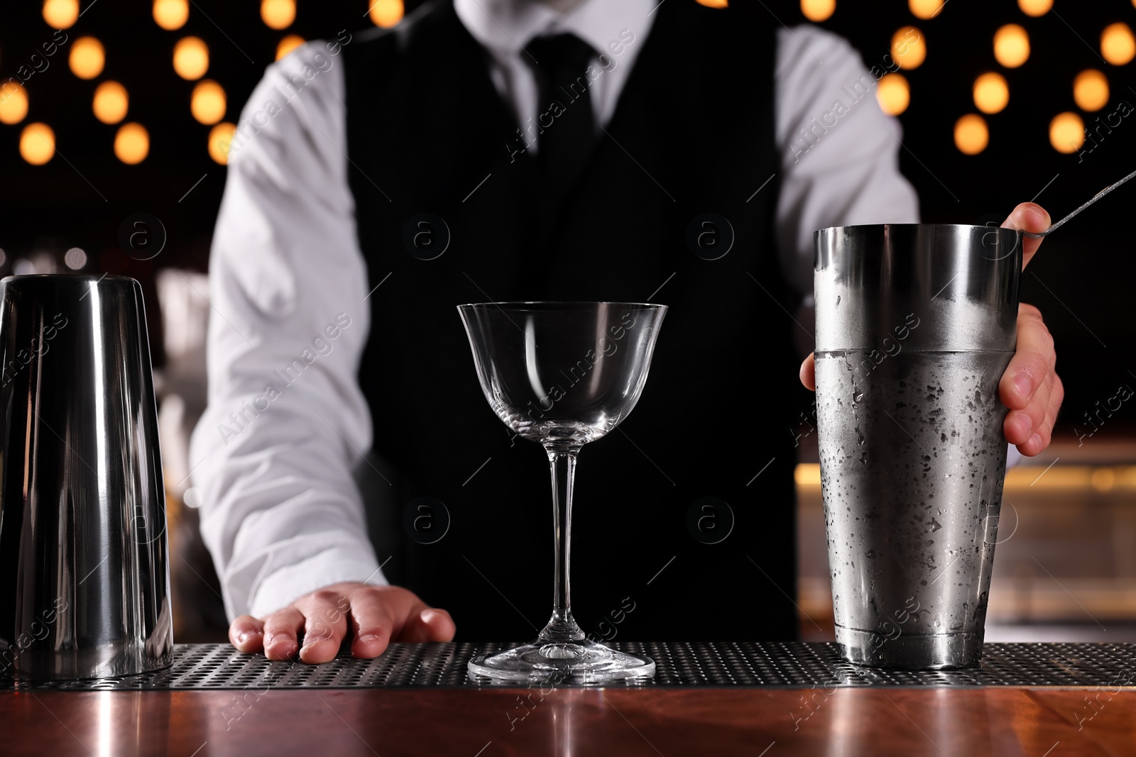 Photo of Bartender with shaker and glass in bar, closeup. Preparing alcoholic cocktail