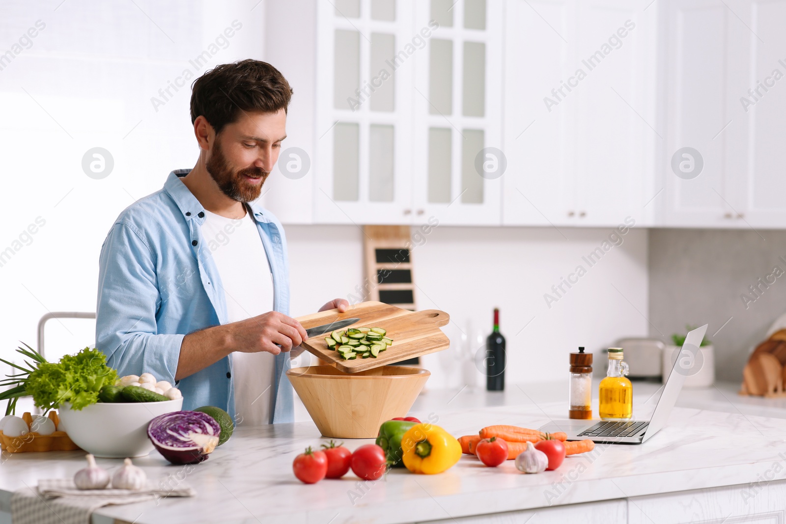 Photo of Man making dinner while watching online cooking course via laptop in kitchen