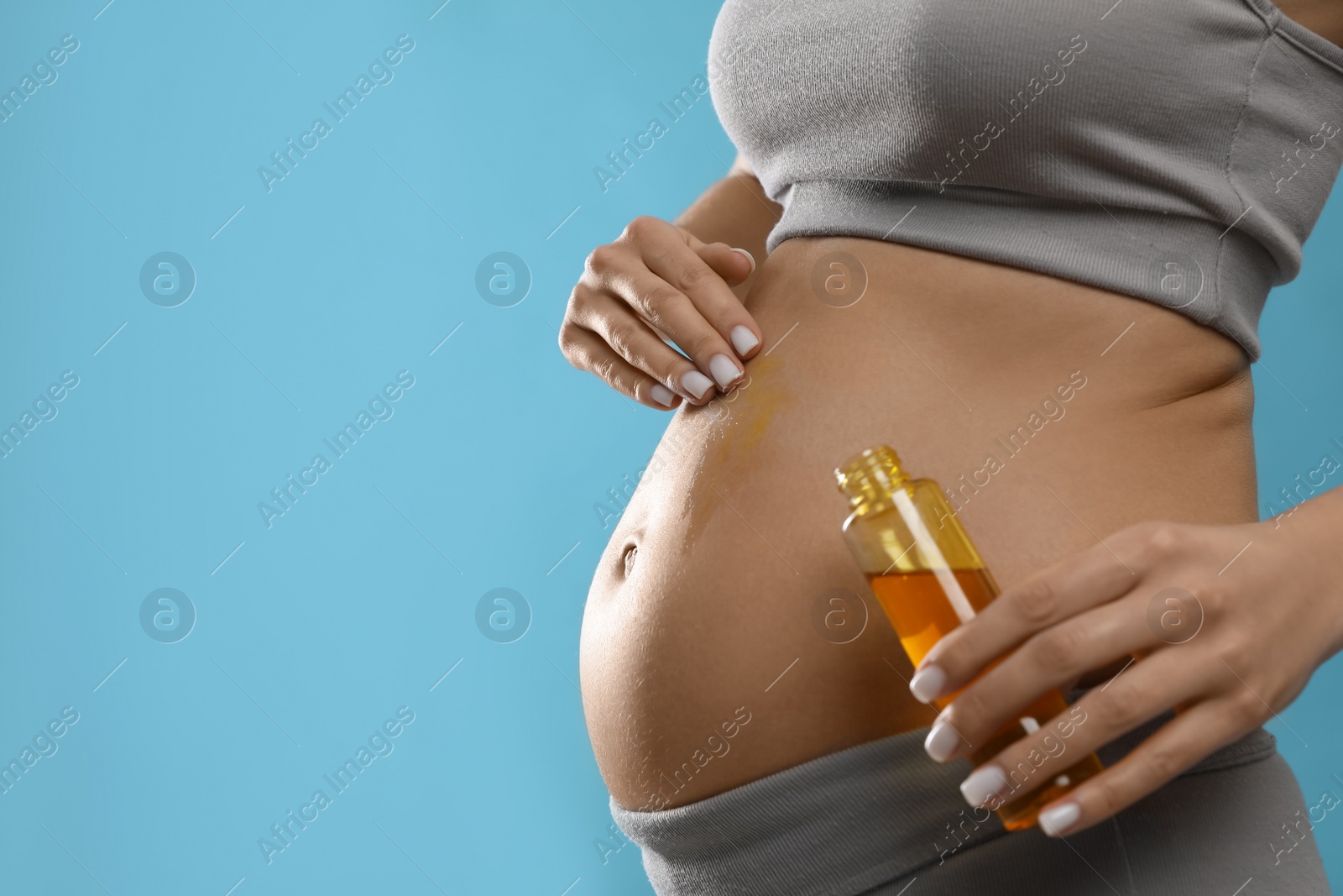 Photo of Pregnant woman applying cosmetic product on belly against light blue background, closeup. Space for text