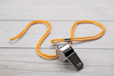 Photo of One metal whistle with cord on light wooden table