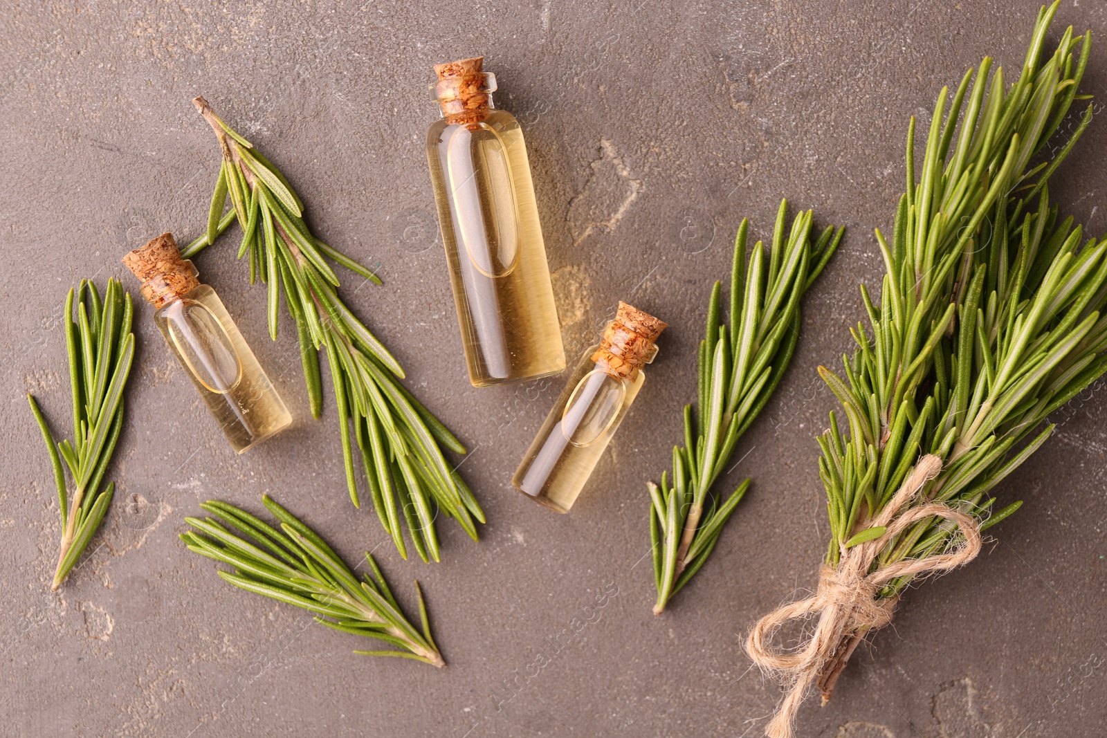 Photo of Essential oil in bottles and rosemary on grey table, flat lay