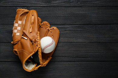 Photo of Catcher's mitt and baseball ball on black wooden table, top view with space for text. Sports game