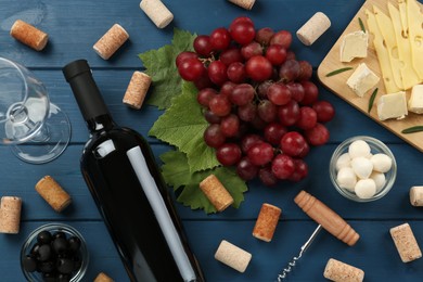 Tasty red wine and snacks on blue wooden table, flat lay