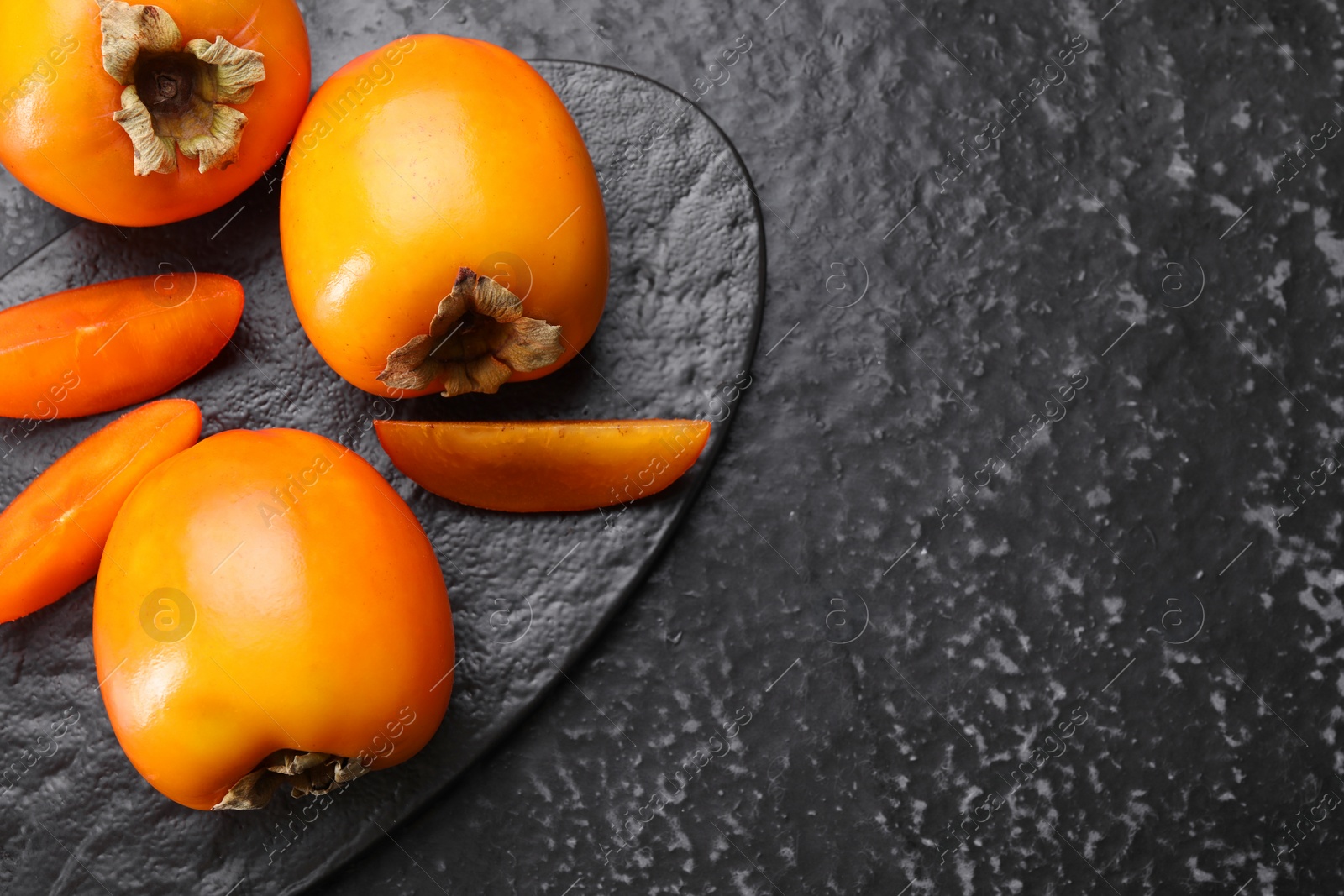 Photo of Delicious ripe persimmons on dark textured table, top view. Space for text