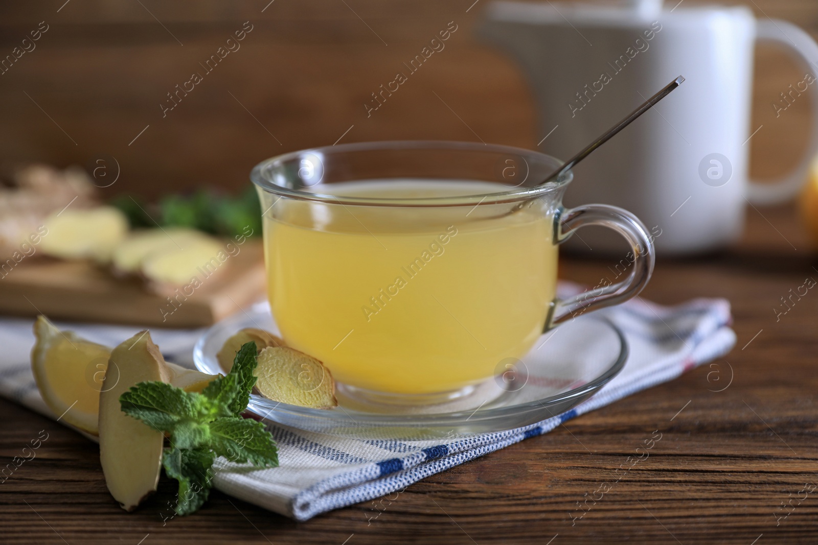 Photo of Glass of aromatic ginger tea and ingredients on wooden table, closeup