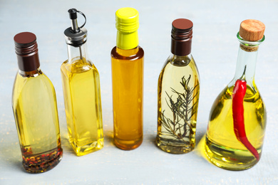 Photo of Different sorts of cooking oil in bottles on grey wooden table
