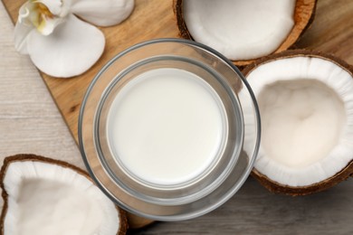 Glass of delicious vegan milk, coconuts and flower on white wooden table, flat lay