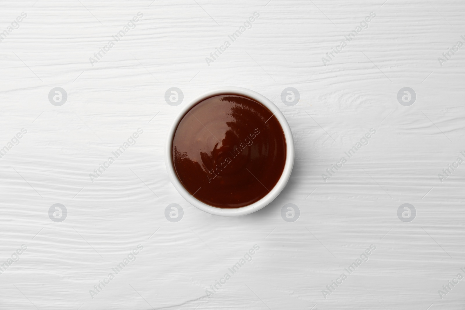 Photo of Tasty barbeque sauce in bowl on white wooden table, top view