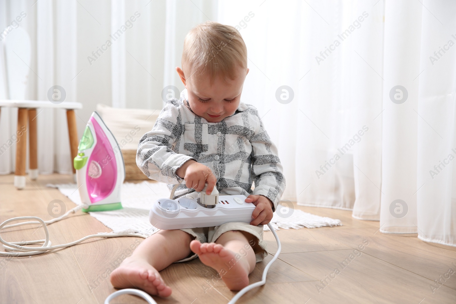 Photo of Little child playing with power strip and iron plug on floor at home. Dangerous situation