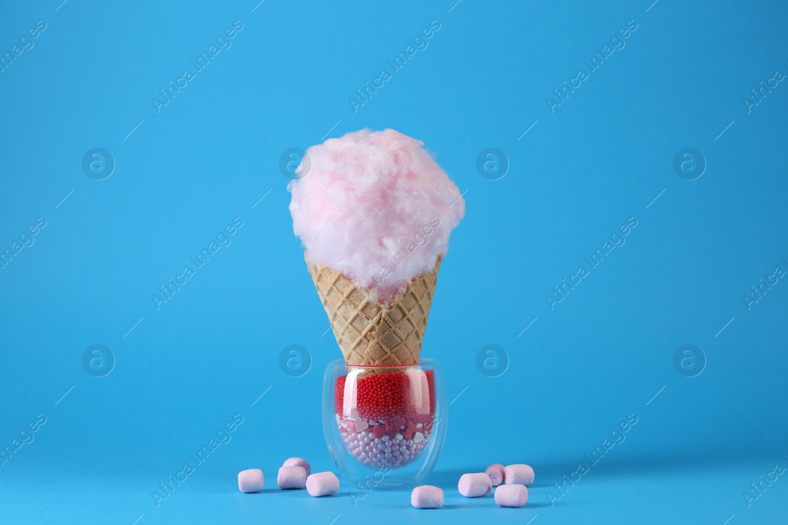 Photo of Sweet cotton candy in waffle cone and marshmallows on light blue background