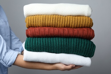 Photo of Woman holding stack of warm clothes on grey background, closeup. Autumn season