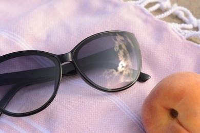 Photo of Beautiful sunglasses and peach on blanket, closeup