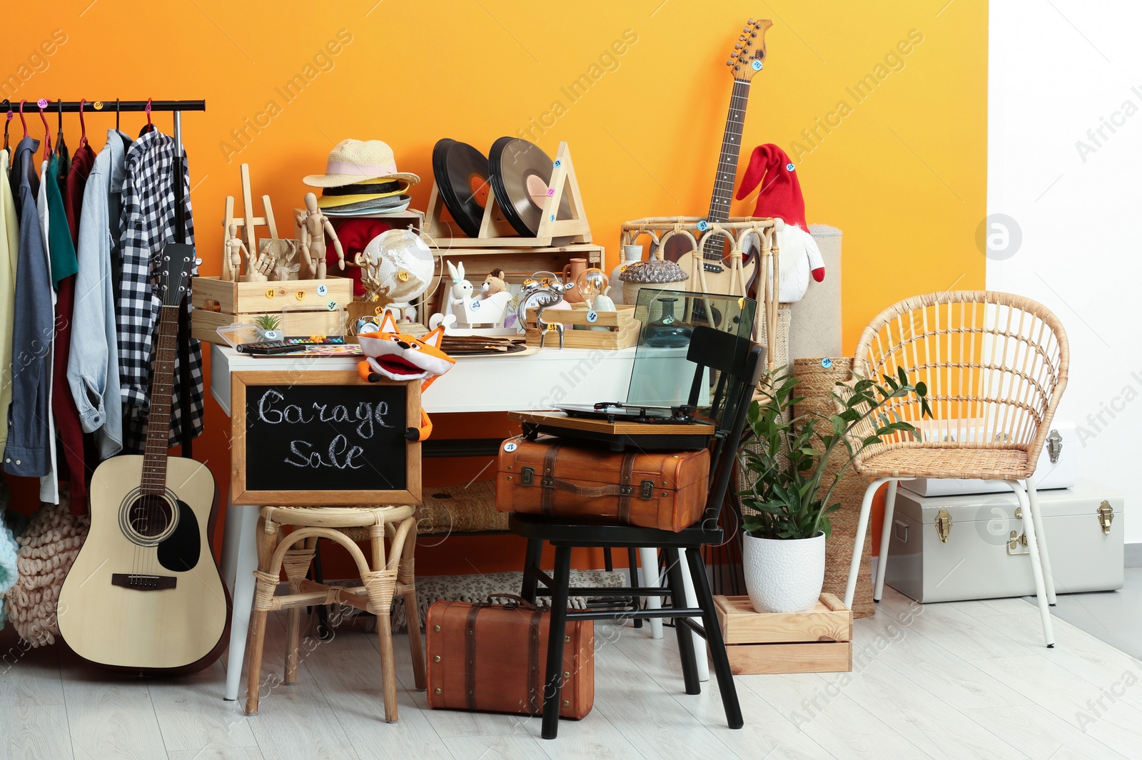 Photo of Sign Garage Sale written on blackboard near many different stuff indoors