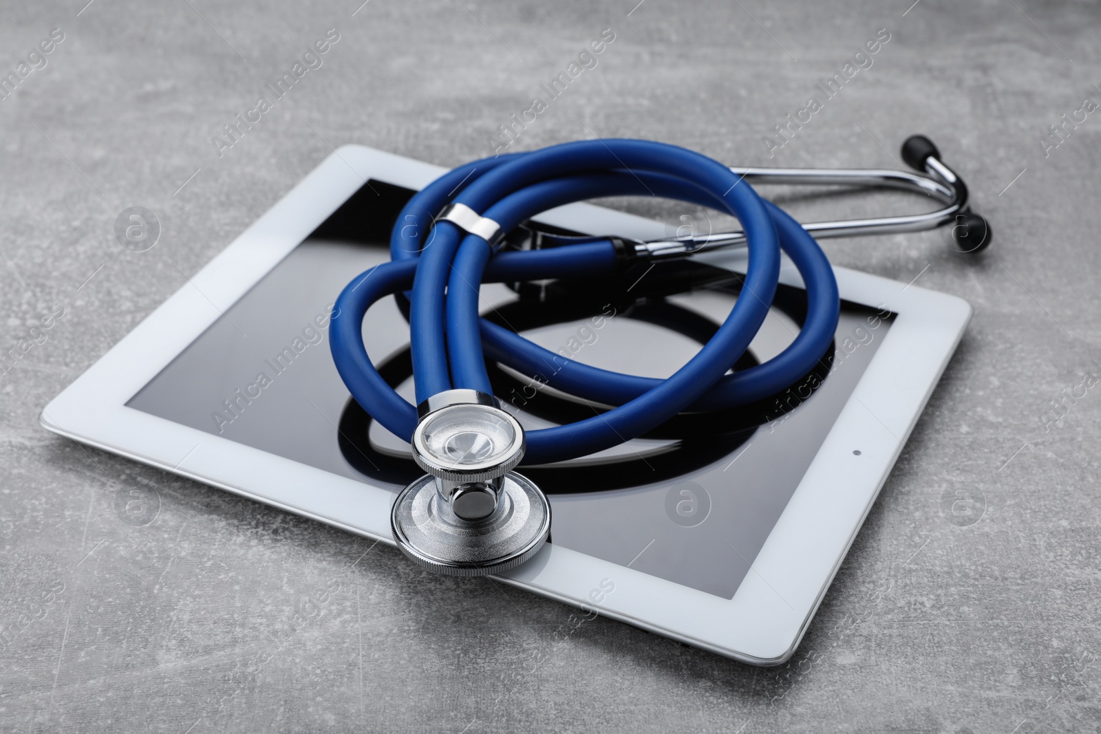 Photo of Computer tablet with stethoscope on grey table