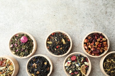 Photo of Different kinds of dry herbal tea in wooden bowls on light grey table, flat lay. Space for text