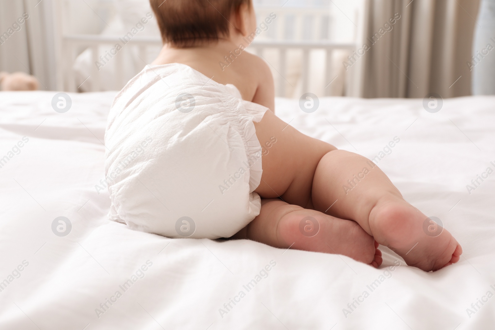 Photo of Little baby in diaper on bed at home, back view