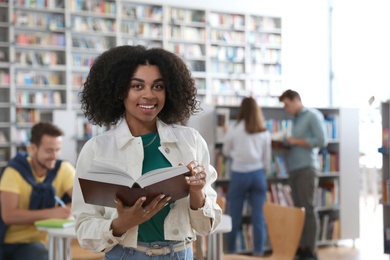 Photo of Young African-American woman with book in library