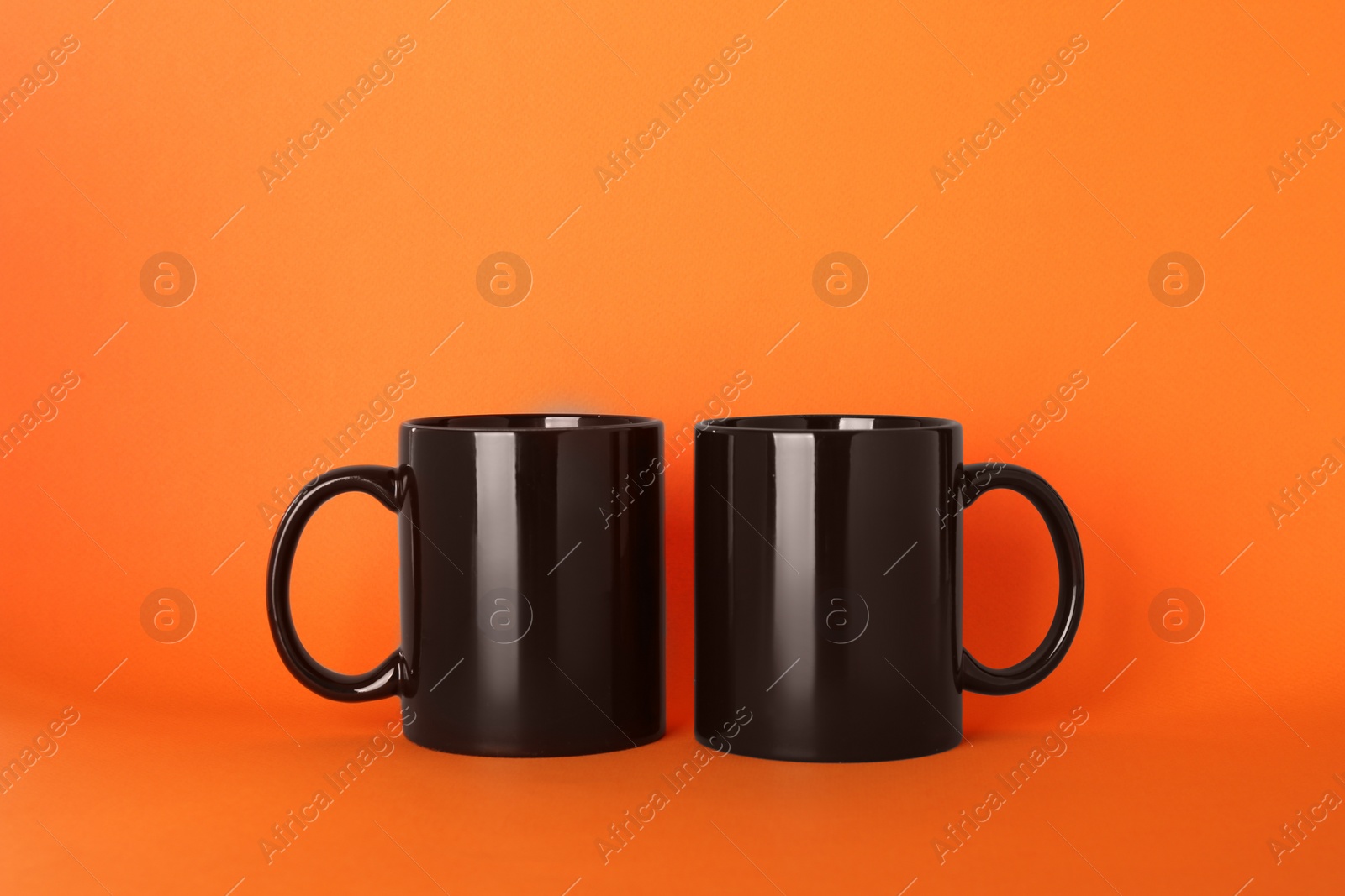 Blank black ceramic mugs on orange background Photo of Blank black ceramic mugs on orange background