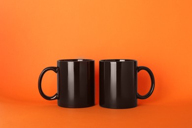 Photo of Blank black ceramic mugs on orange background