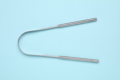 Photo of Metal tongue cleaner on light blue background, top view