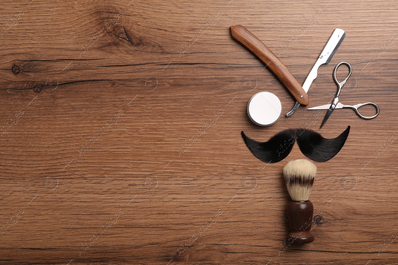 Photo of Artificial moustache and barber tools on wooden table, flat lay. Space for text