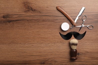 Artificial moustache and barber tools on wooden table, flat lay. Space for text