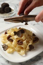 Photo of Woman slicing truffle onto tagliatelle at white marble table, closeup