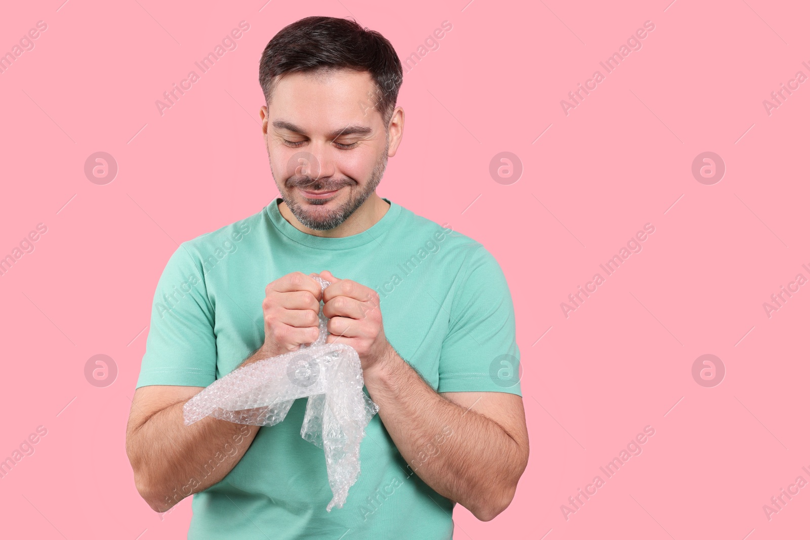 Photo of Happy man with bubble wrap on pink background. Space for text