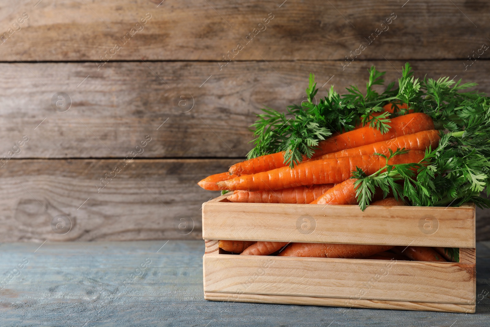 Photo of Crate of fresh carrots on wooden background. Space for text