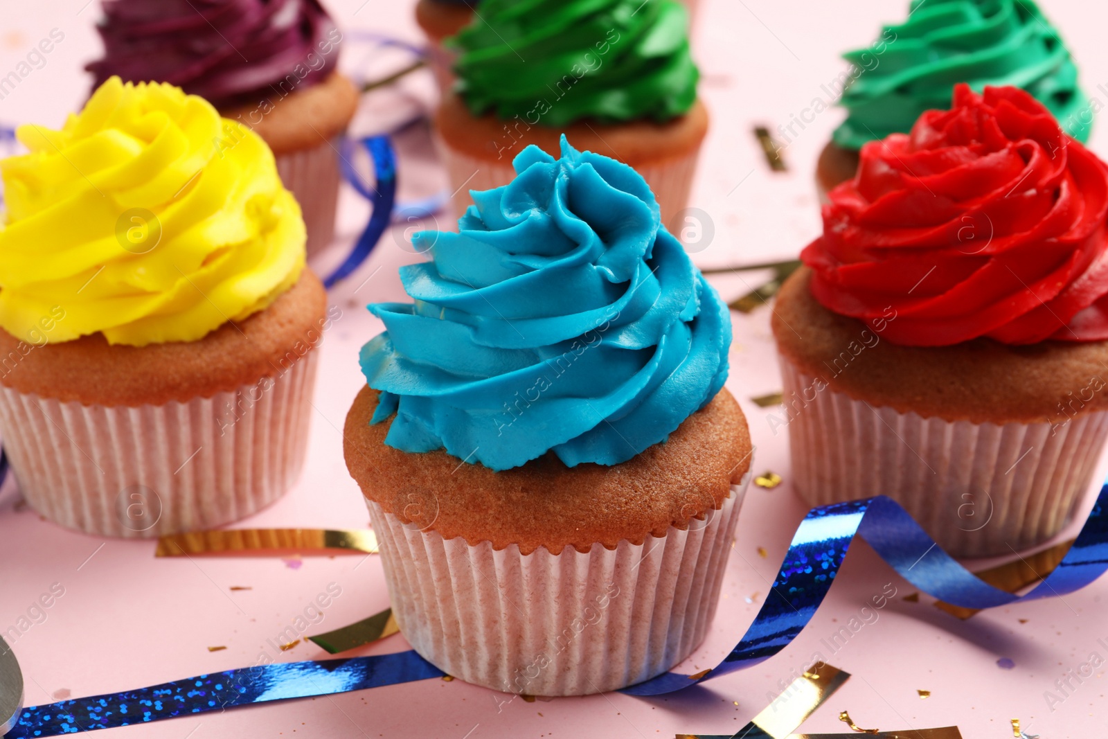 Photo of Many delicious colorful cupcakes and confetti on pink table, closeup