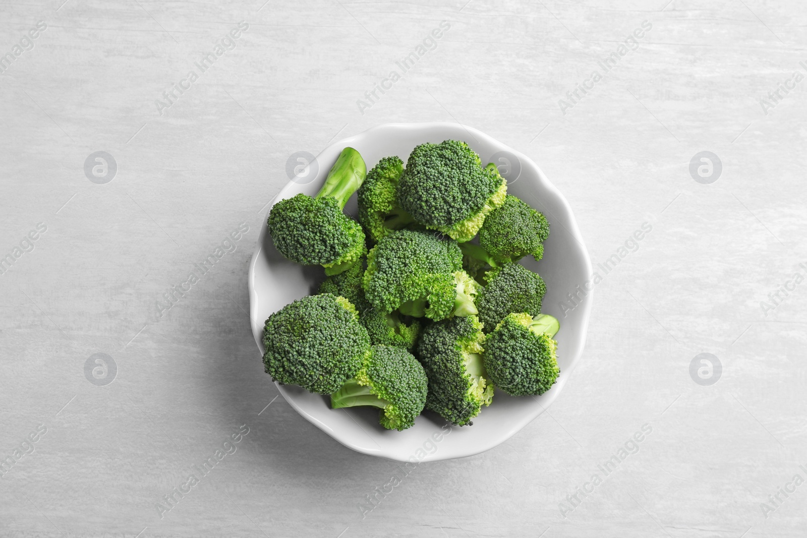 Photo of Bowl of fresh broccoli on light grey table, top view