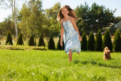 Beautiful girl walking with cute Maltipoo dog on green lawn in park