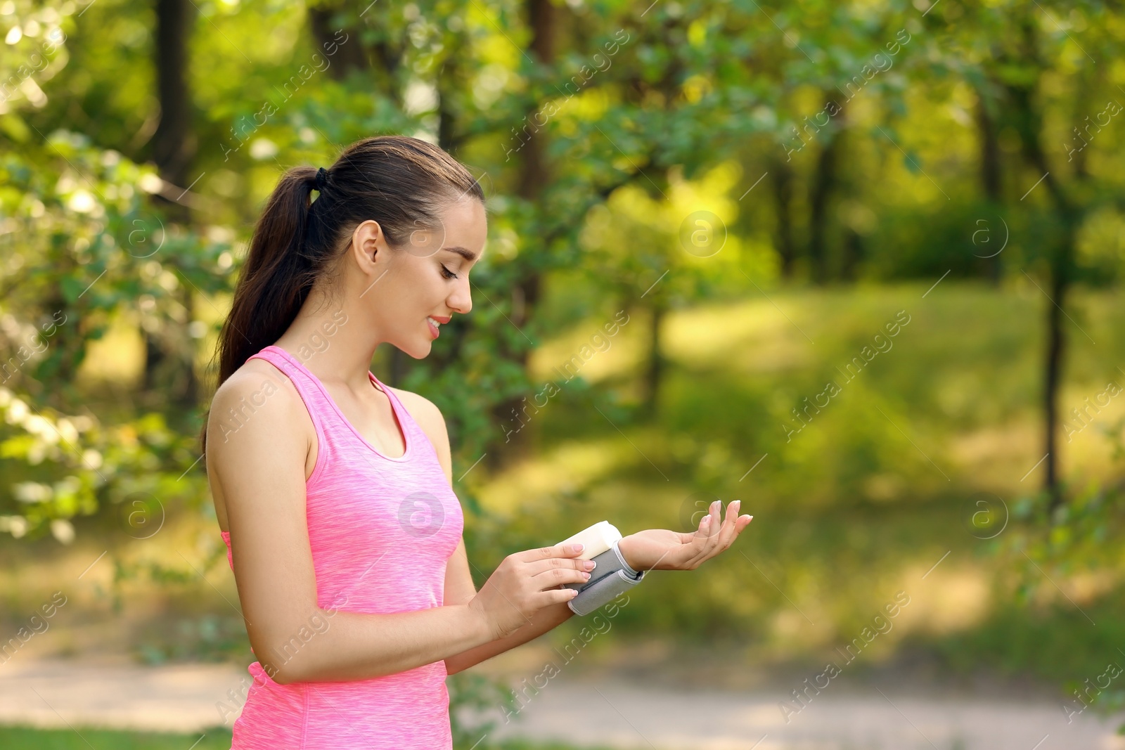 Photo of Young woman checking pulse outdoors on sunny day