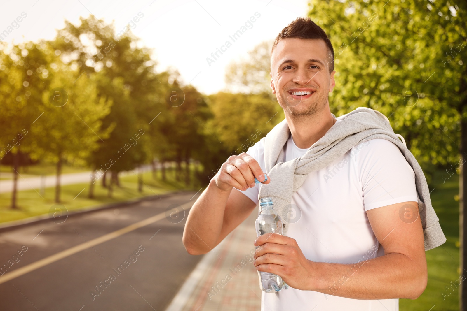 Photo of Young man with bottle of water outdoors. Morning fitness