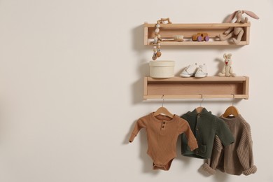 Wooden shelves with baby clothes, toys and accessories on white wall. Space for text