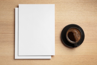 Photo of Blank paper sheets for brochure and cup of coffee on wooden background, flat lay. Mock up