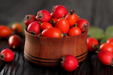 Photo of Ripe rose hip berries with green leaves on black wooden table, closeup